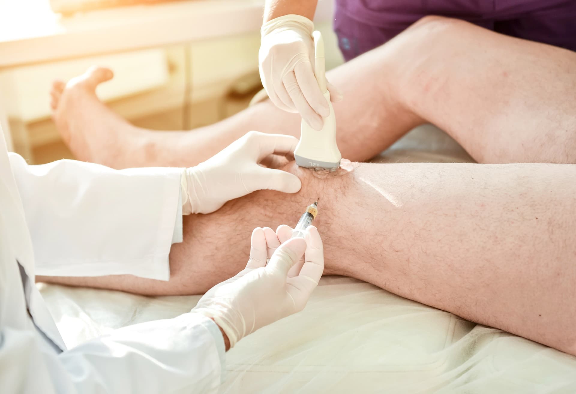 Ultrasound-guided knee injection, with the probe held on the knee while the needle is placed